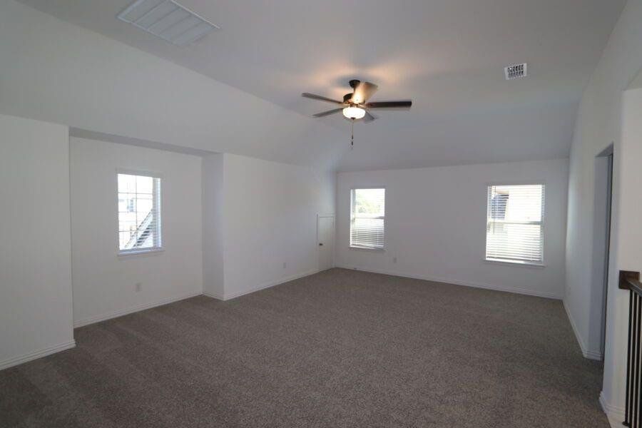 Carpeted empty room featuring vaulted ceiling and ceiling fan