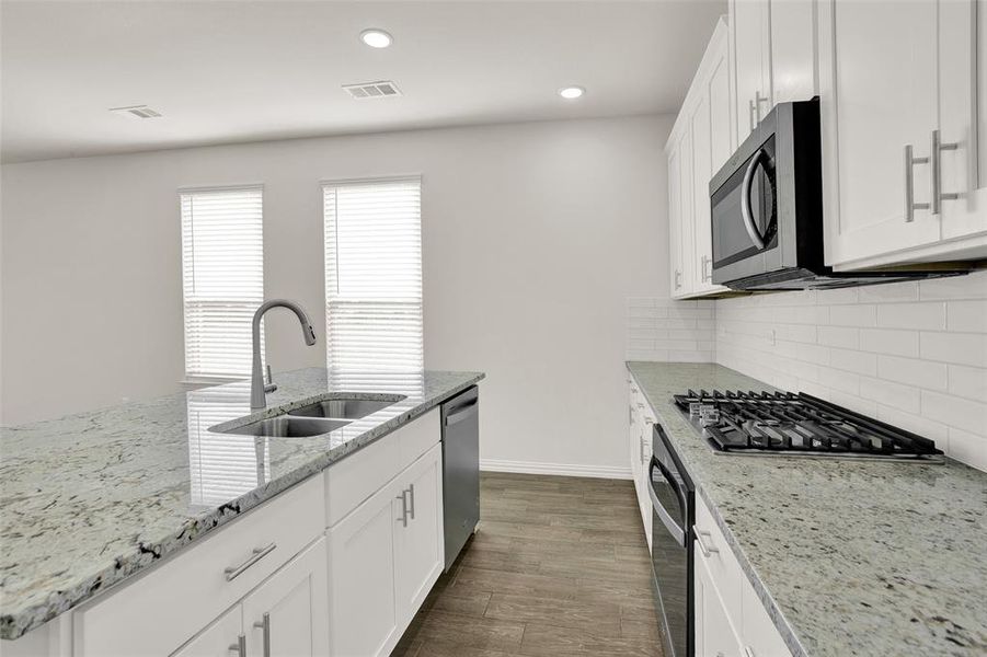 Kitchen featuring dark wood-type flooring, stainless steel appliances, white cabinets, sink, and tasteful backsplash