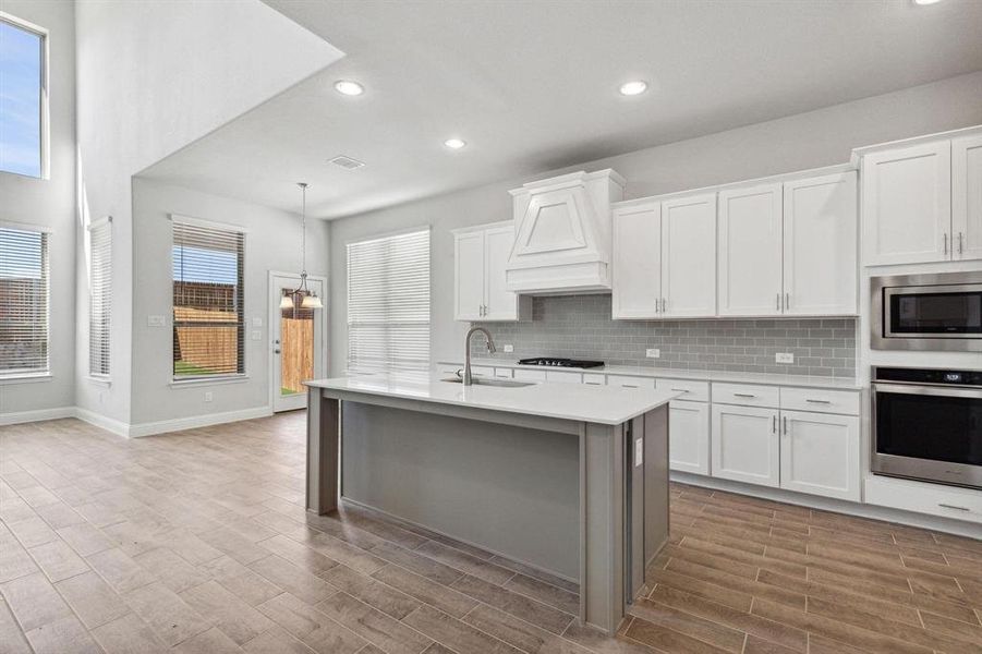 Kitchen featuring wood-type flooring, sink, white cabinets, hanging light fixtures, and appliances with stainless steel finishes