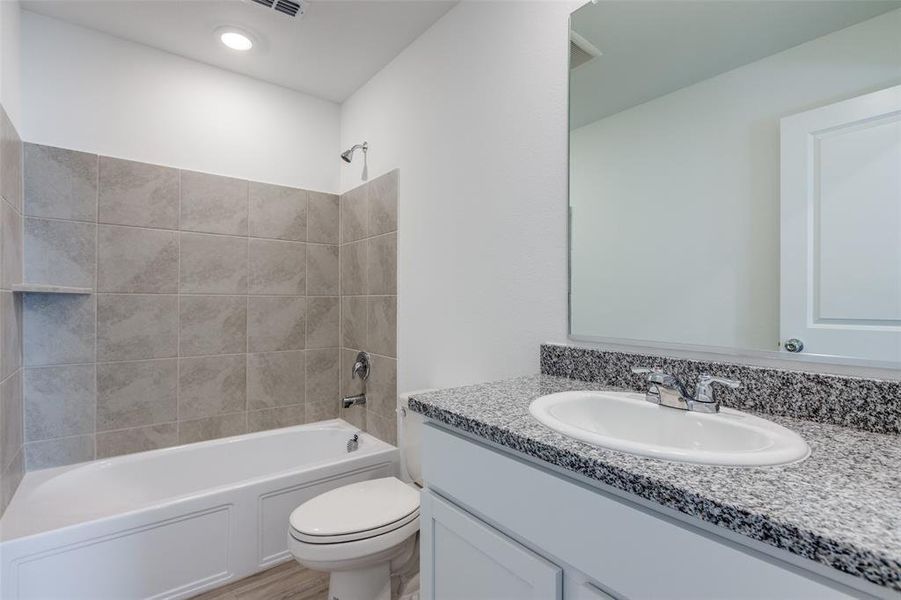 Full bathroom featuring vanity, hardwood / wood-style floors, tiled shower / bath combo, and toilet