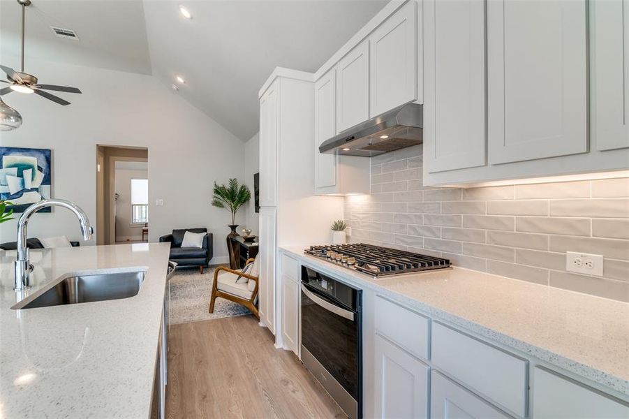 This view shows the 5-burner gas stove top with a large oven below.  The hood over the stove vents to the out side and there are ample white cabinets throughout.