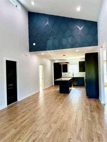 Kitchen featuring a towering ceiling, light hardwood / wood-style flooring, a center island, and backsplash