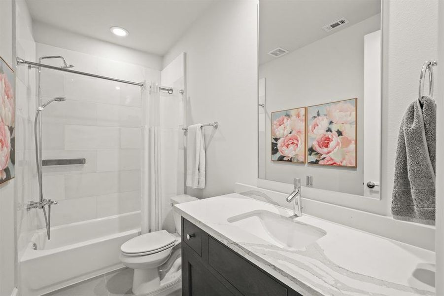 Secondary bathroom complete with a mirror, quartz countertops and wooden cabinets, tile floors, recessed lighting, and a shower/tub combo with a gorgeous tile shower wall.