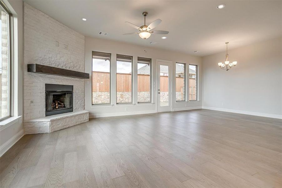 Unfurnished living room featuring light hardwood / wood-style floors, ceiling fan with notable chandelier, and a stone fireplace