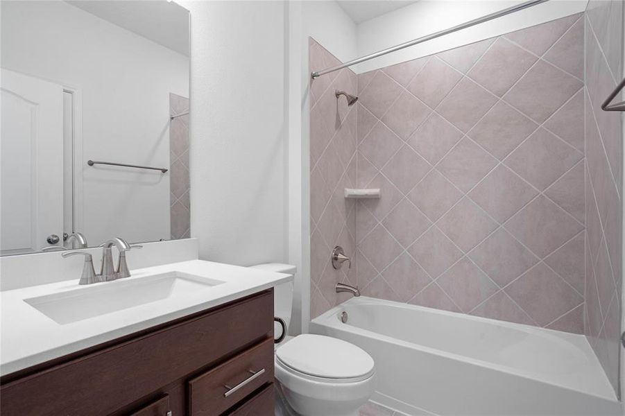 Secondary bath features tile flooring, bath/shower combo with tile surround, strained wood cabinets, beautiful light countertops, mirror, dark, sleek fixtures and modern finishes!