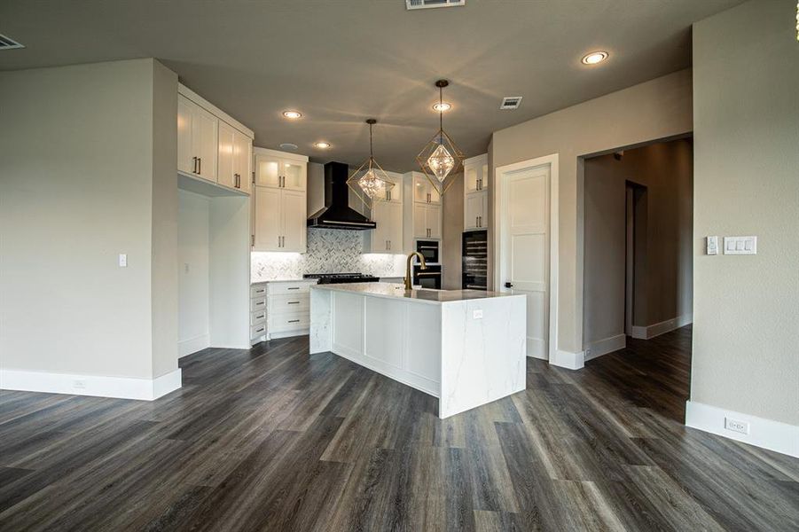 Kitchen featuring tasteful backsplash, white cabinets, wall chimney range hood, an island with sink, and dark hardwood / wood-style flooring
