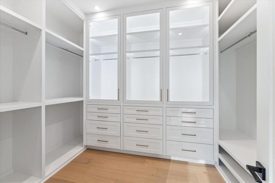 PRIMARY CLOSET #1: As you step into the spacious closet, you're greeted by sleek glass front doors with lighting. Custom-built shelving and cabinetry offer abundant storage options, ensuring that everything from clothing and shoes to handbags and accessories can be neatly stowed away and easily accessible whenever needed.