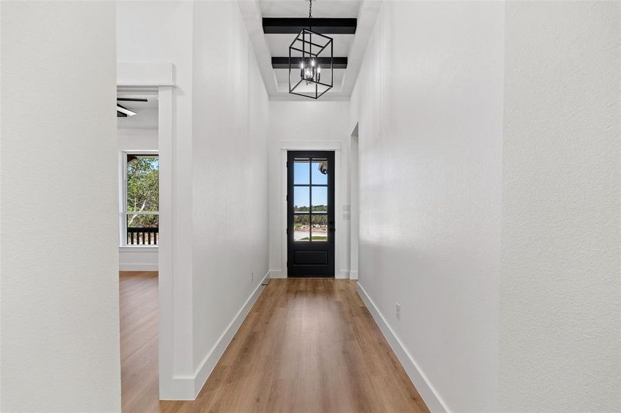 Doorway to outside featuring ceiling fan with notable chandelier, light wood-type flooring, and a towering ceiling