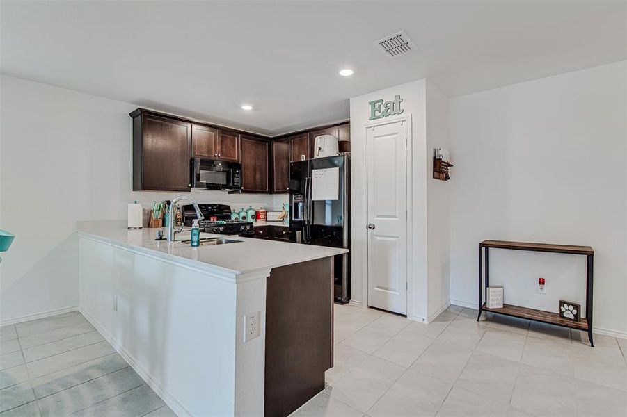 Kitchen featuring sink, stainless steel range with electric stovetop, kitchen peninsula, dark brown cabinetry, and refrigerator with ice dispenser