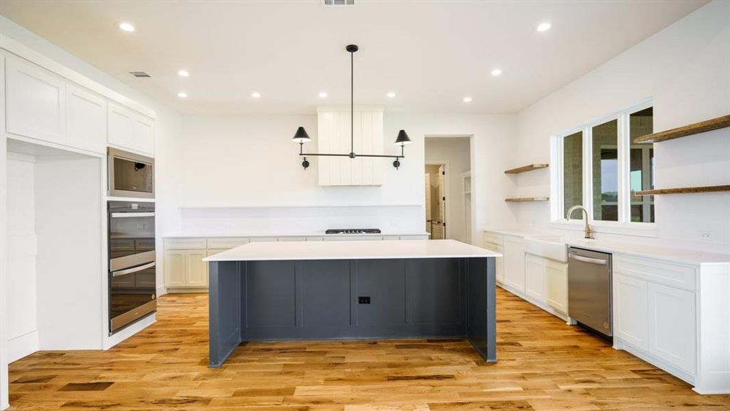 Kitchen featuring pendant lighting, white cabinetry, appliances with stainless steel finishes, and light hardwood / wood-style flooring