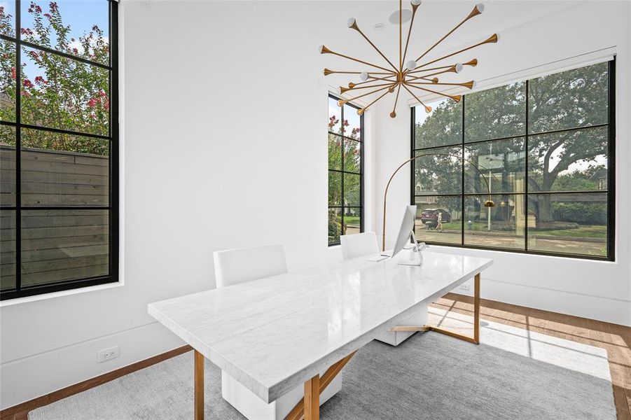 This bright and airy study features sleek hardwood floors and a high ceiling, creating a spacious feel. The striking contemporary light fixture adds a modern touch, while large windows offer scenic views of the front yard.