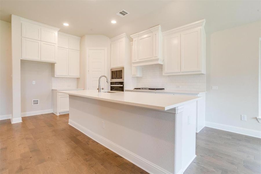 Kitchen with decorative backsplash, light hardwood / wood-style flooring, a kitchen island with sink, and white cabinets