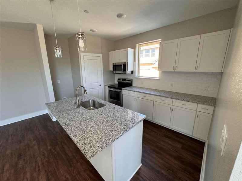 Kitchen with appliances with stainless steel finishes, a center island with sink, sink, and decorative light fixtures