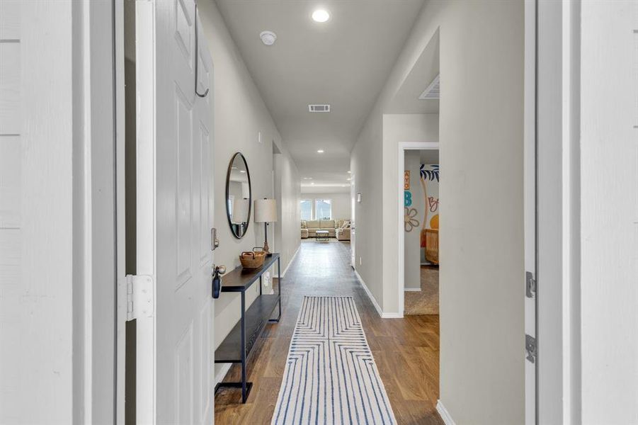 Inviting entry hallway with wood-like vinyl flooring and modern accents leads to a bright, open living area