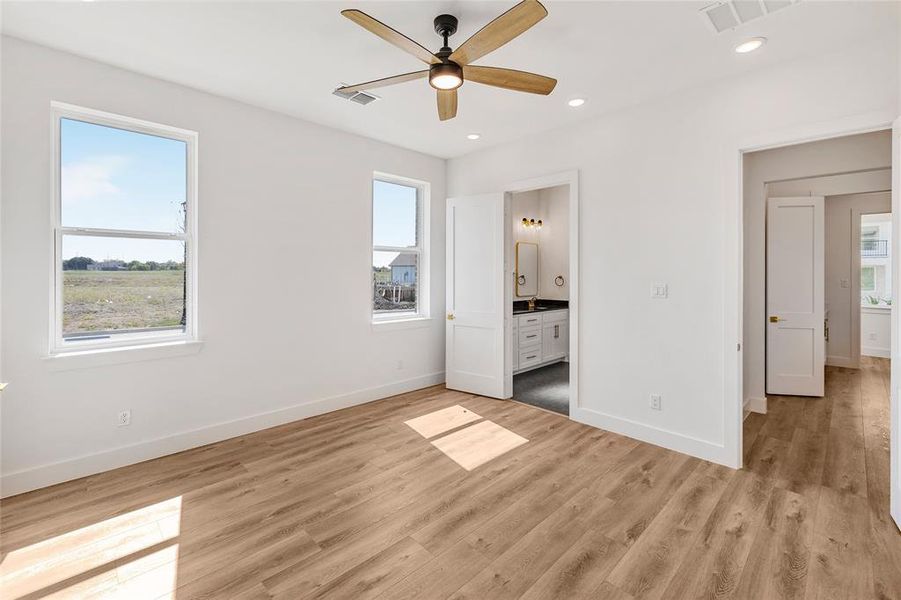 Unfurnished bedroom with light hardwood / wood-style flooring, multiple windows, and ensuite bath