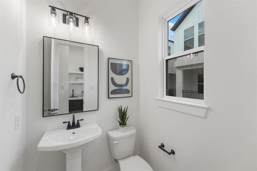 Your modern half-bathroom comes completed with custom paint, featuring a pedestal sink, and a modern framed black matte mirror with overhead lighting. A window allows for rays natural lighting.