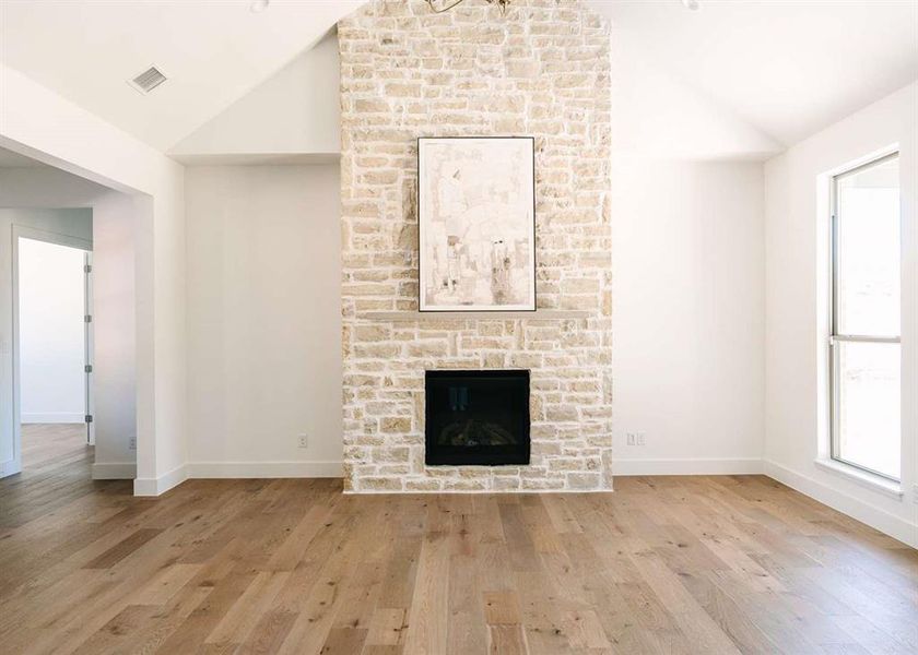 Unfurnished living room with vaulted ceiling, a fireplace, and light hardwood / wood-style flooring