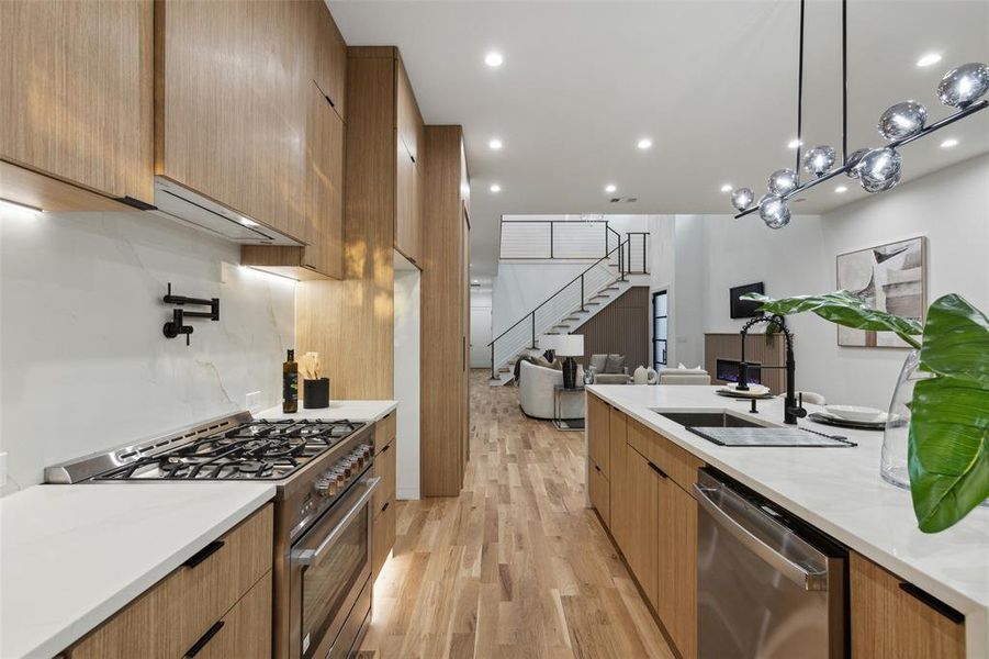 Kitchen featuring light hardwood / wood-style flooring, appliances with stainless steel finishes, premium range hood, decorative light fixtures, and a chandelier