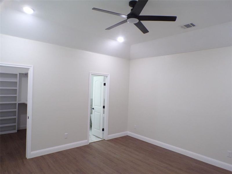 Unfurnished bedroom with a spacious closet, dark wood-type flooring, ceiling fan, and a closet
