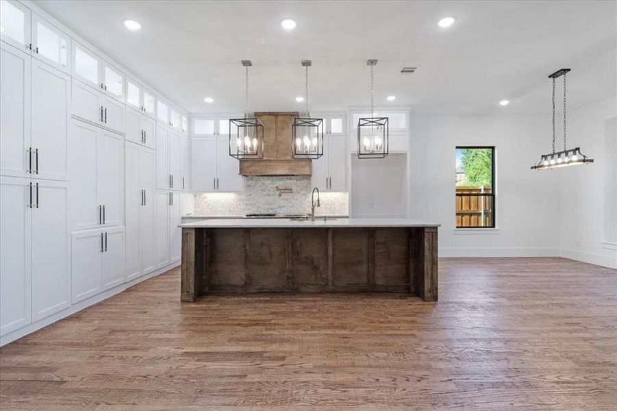 Kitchen featuring white cabinetry, a center island with sink, hardwood / wood-style flooring, decorative light fixtures, and tasteful backsplash