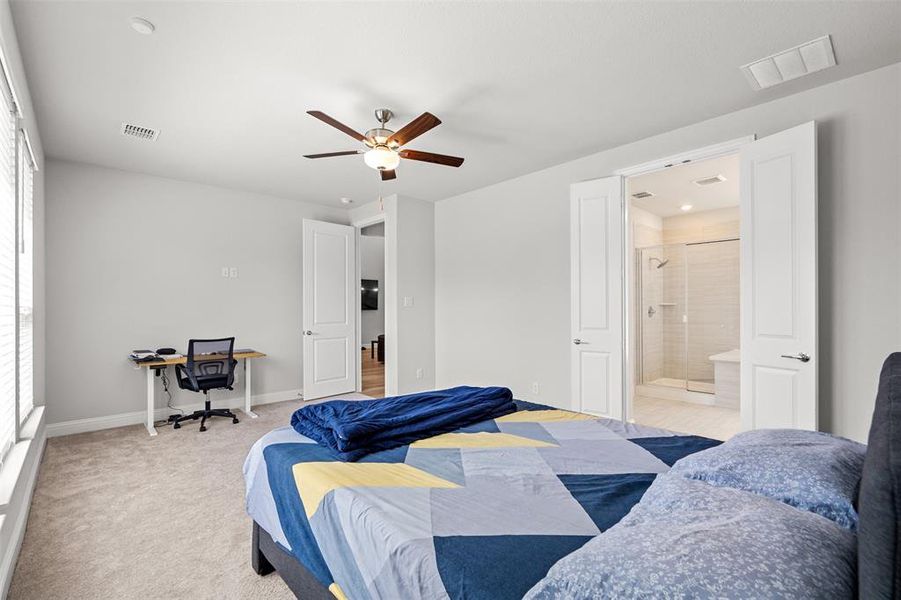 Carpeted bedroom featuring ceiling fan, ensuite bathroom, and multiple windows