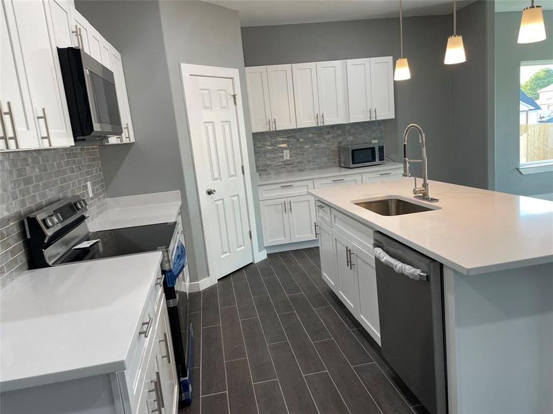 Kitchen with sink, stainless steel appliances, decorative light fixtures, and white cabinets