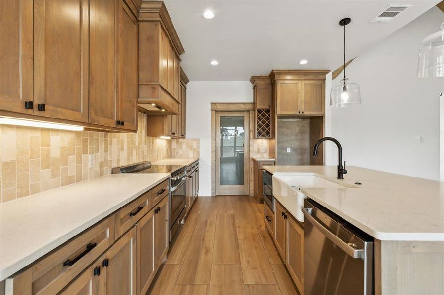 Kitchen with light wood-type flooring, decorative light fixtures, stainless steel appliances, sink, and light stone countertops