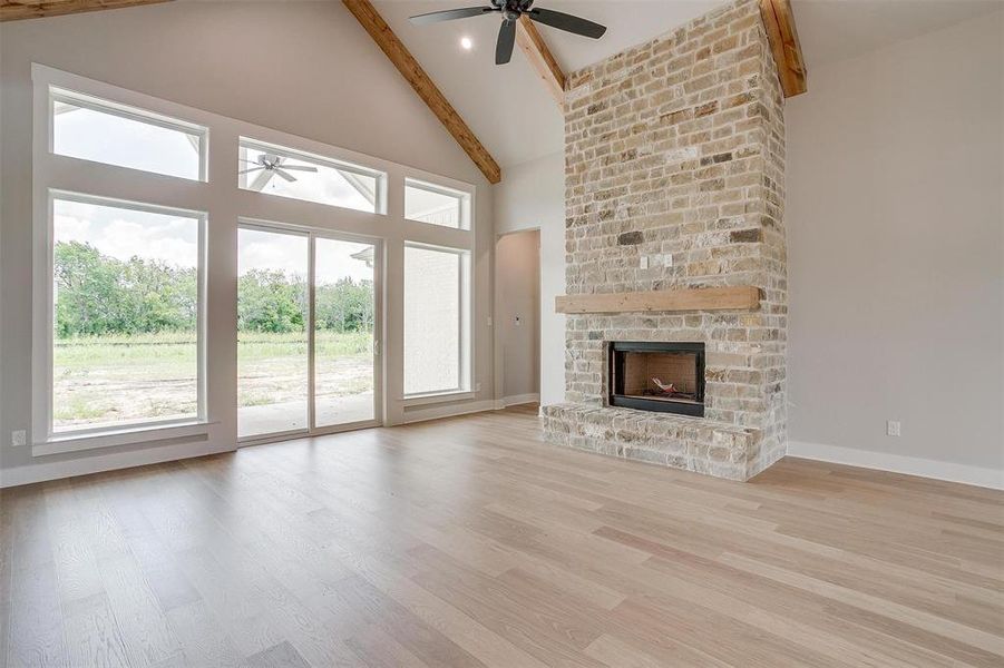 Unfurnished living room featuring beamed ceiling, ceiling fan, light hardwood / wood-style flooring, and a large fireplace