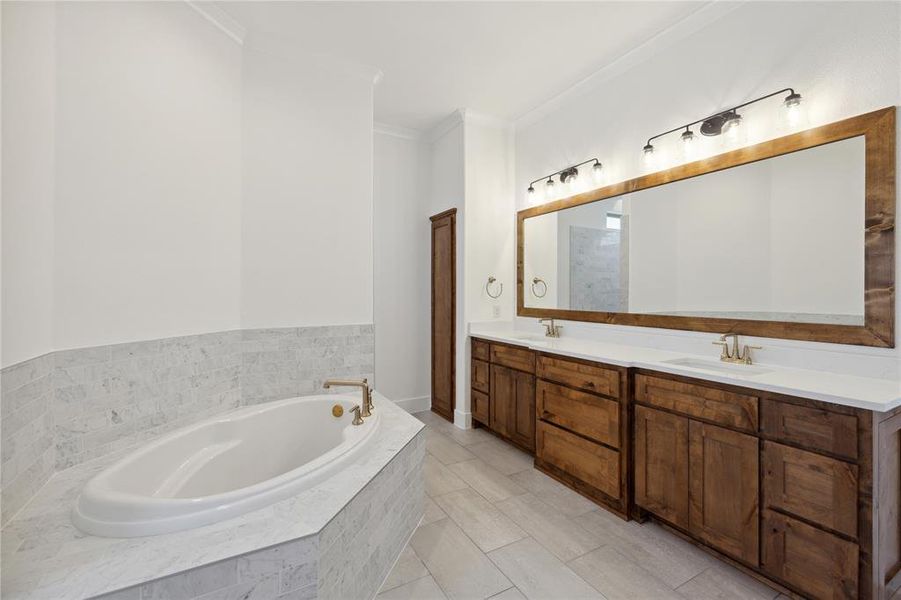 Bathroom featuring tiled tub, dual vanity, tile patterned flooring, and crown molding