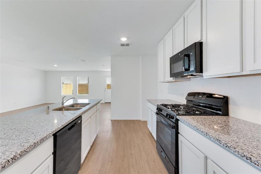 Kitchen with light hardwood / wood-style floors, white cabinets, black appliances, and sink