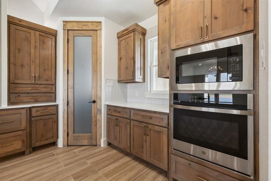 Kitchen featuring stainless steel oven, tasteful backsplash, black microwave, and light wood-type flooring