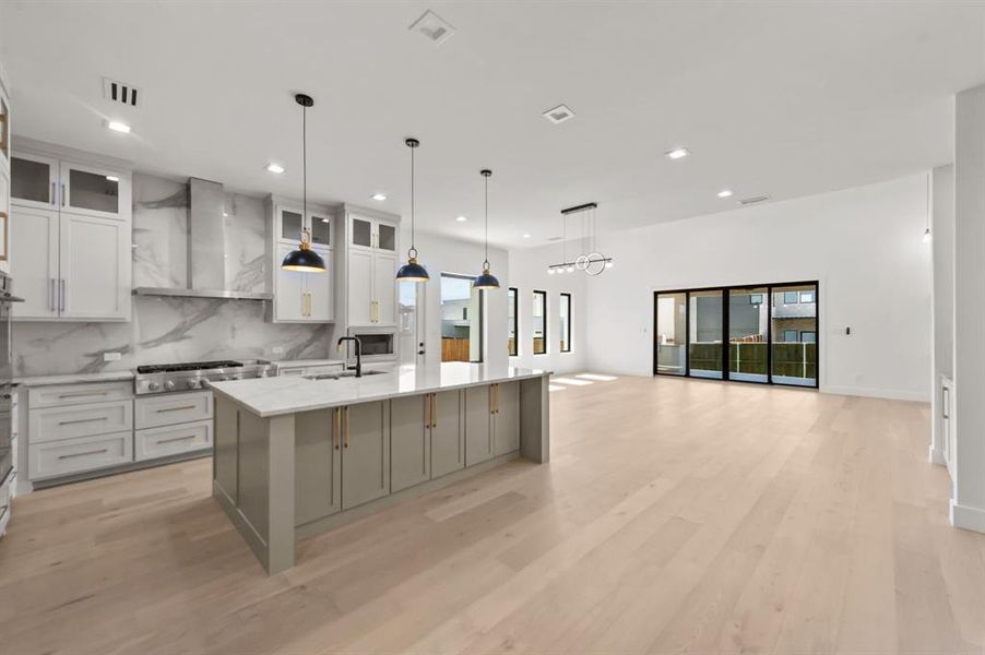 Kitchen with light wood-type flooring, wall chimney exhaust hood, stainless steel gas stovetop, and a spacious island