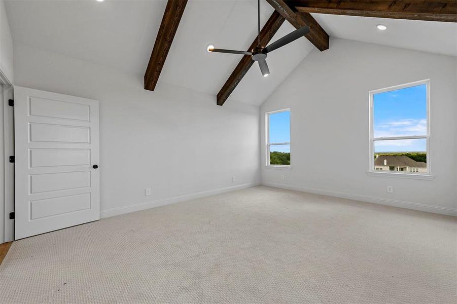 Carpeted empty room with ceiling fan, beam ceiling, a healthy amount of sunlight, and high vaulted ceiling