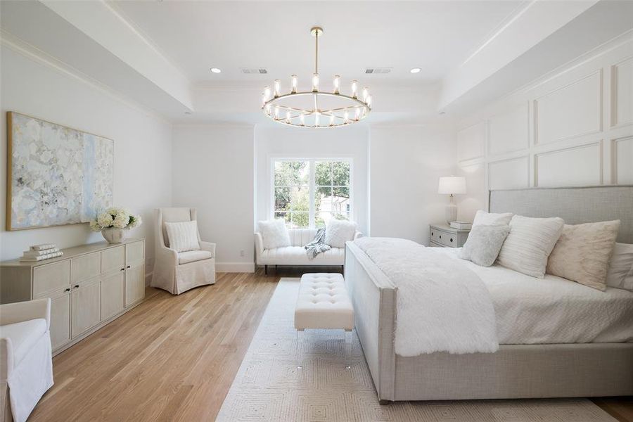 Bedroom featuring an inviting chandelier, light wood flooring, and a raised ceiling