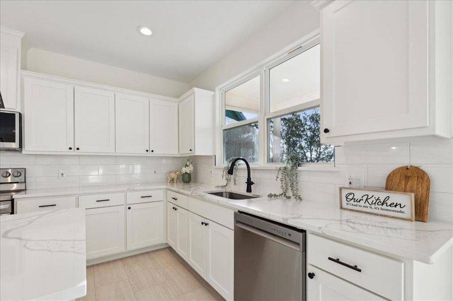 Kitchen featuring appliances with stainless steel finishes, white cabinets, sink, and tasteful backsplash