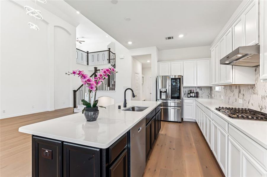 Kitchen featuring appliances with stainless steel finishes, light wood-type flooring, ventilation hood, a kitchen island with sink, and sink