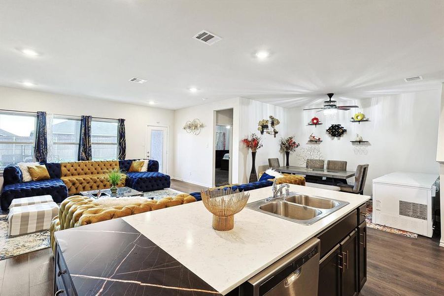 Kitchen featuring dishwasher, a center island with sink, light stone counters, and dark wood-type flooring