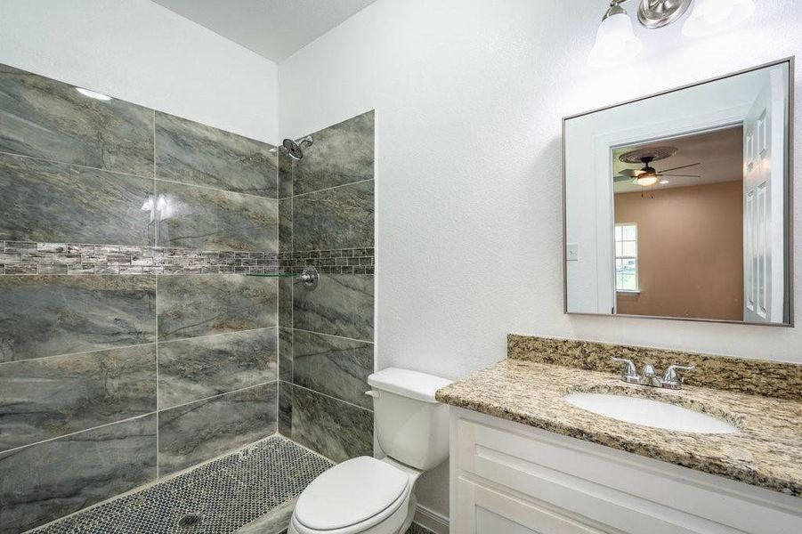 Bathroom with vanity, tiled shower, ceiling fan, and toilet