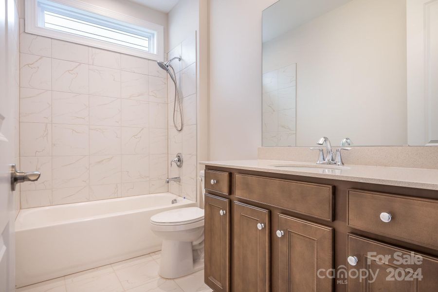 Secondary Bath with upgraded cabinetry, quartz countertops, tile floors and tile-surround tub with handheld shower is conveniently located near the front of the home for easy access by your guests.
