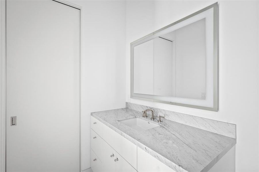 The ensuite bath showcases a Duravit shower/tub combo adorned with beautiful blue-gray linear tiles, paired with limestone flooring. A front-lit mirror and Carrera marble countertops complete the elegant design of this modern space.