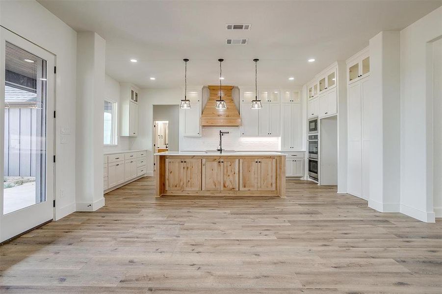 Kitchen featuring a center island with sink, light brown cabinets, custom exhaust hood, light wood-type flooring, and white cabinets