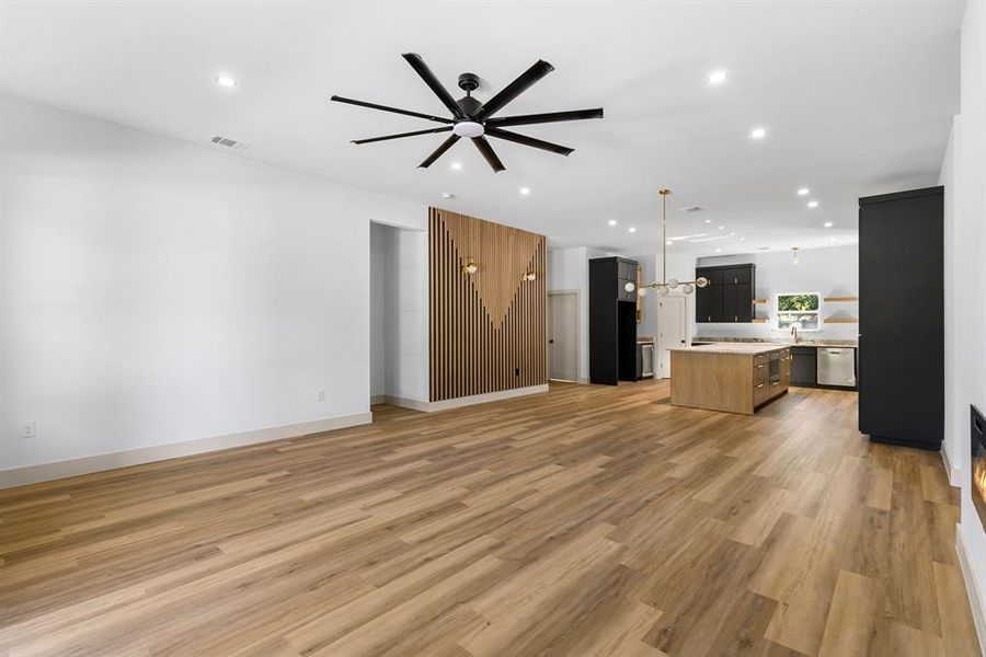 Unfurnished living room with ceiling fan with notable chandelier, sink, and light hardwood / wood-style floors