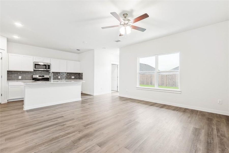 Kitchen featuring range, white cabinets, backsplash, a kitchen island with sink, and light hardwood / wood-style floors