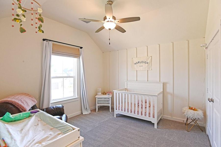 Carpeted bedroom featuring a crib, ceiling fan, and lofted ceiling
