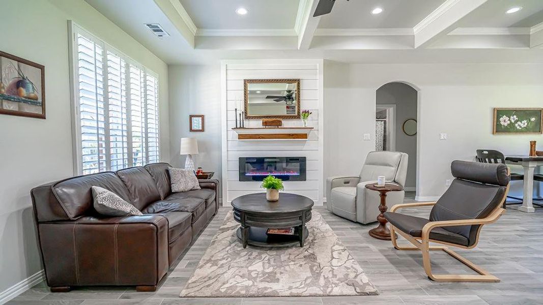 Living room with a fireplace, crown molding, beam ceiling, and light hardwood / wood-style flooring