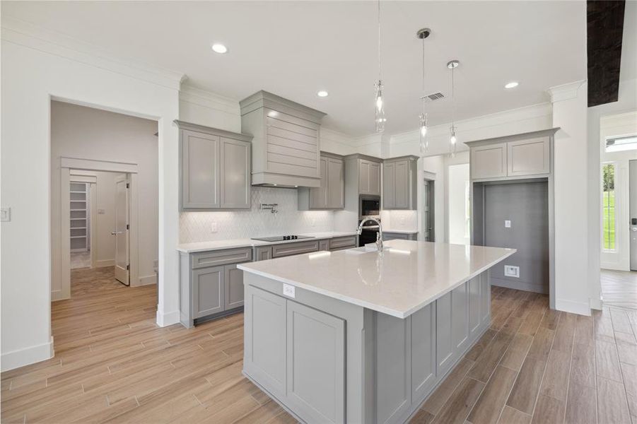 Kitchen with gray cabinets, decorative light fixtures, a center island with sink, and light hardwood / wood-style flooring