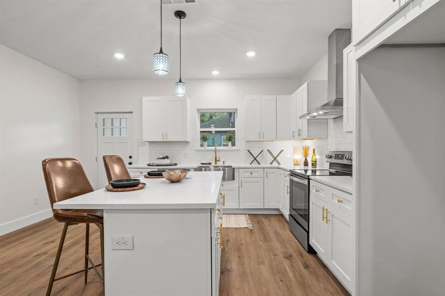 Kitchen featuring white cabinets, a kitchen breakfast bar, stainless steel electric range oven, wall chimney exhaust hood, and a center island