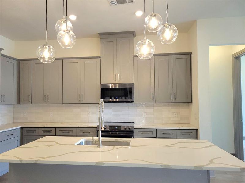 Kitchen with a center island with sink, hanging light fixtures, tasteful backsplash, and light stone counters