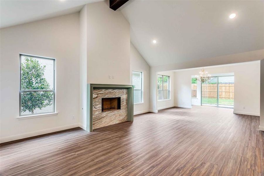 Unfurnished living room featuring beamed ceiling, hardwood / wood-style floors, a stone fireplace, high vaulted ceiling, and a notable chandelier