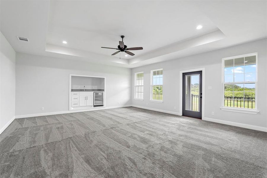 Unfurnished living room with wine cooler, ceiling fan, a tray ceiling, and carpet floors